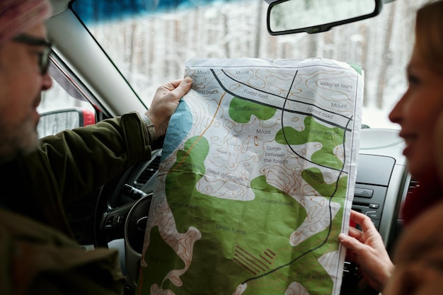 Concentre-se no mapa de papel local mantido por marido e mulher maduros viajando de carro