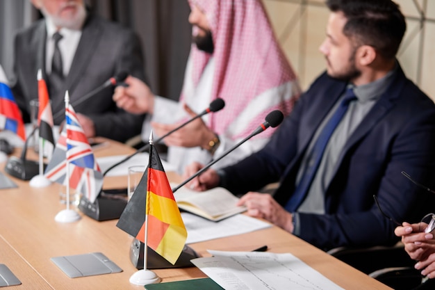 Concéntrese en la bandera de mesa alemana durante la reunión, foto de primer plano. Personas ejecutivas recortadas sentadas en conferencia de prensa, reunión sin ataduras