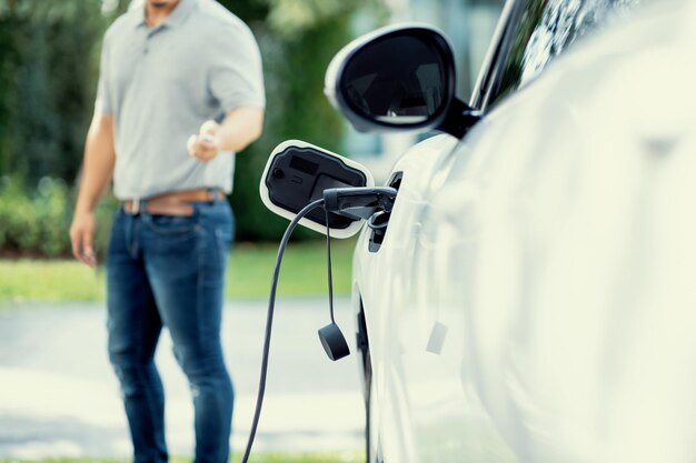 Concéntrese en cargar el coche EV con un fondo borroso de un hombre parado en un EV progresivo