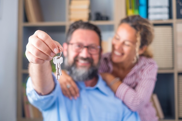 Concéntrese en las llaves en poder de los emocionados jóvenes cónyuges propietarios de viviendas Feliz pareja familiar casada celebrando mudarse a una nueva casa demostrando las llaves de pie en el concepto de hipoteca de bienes raíces del apartamentoxA