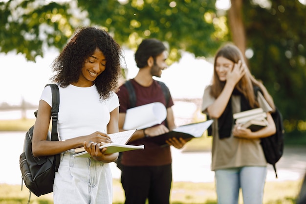 Concéntrese en una niña africana que está de pie por separado. Grupo de estudiantes internacionales parados juntos en el parque en la universidad