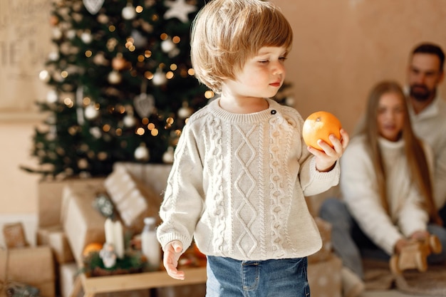 Concéntrese en un niño que sostiene una mandarina y sus padres en un fondo