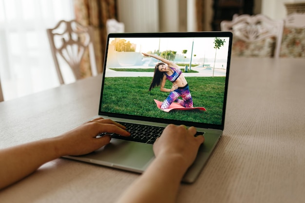 Concéntrese en la pantalla de la computadora portátil con una mujer joven en ropa deportiva haciendo ejercicios matutinos sentadillas profundas en una alfombra de yoga manteniéndose en forma en casa Chica interesada viendo capacitación en talleres educativos de fitness en línea
