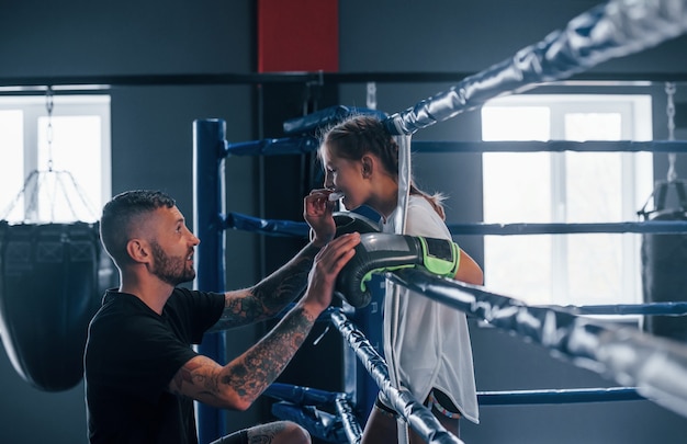 Concepción de la asistencia. Entrenador de boxeo tatuado joven enseña a niña linda en el gimnasio.