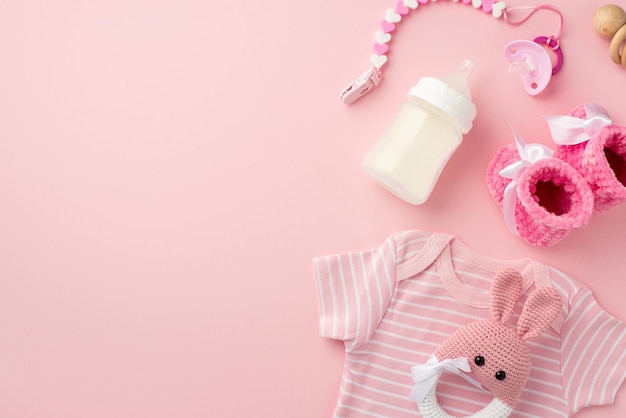 Concepto de accesorios para bebés Foto de vista superior de ropa infantil camisa rosa botines de bebé cadena de chupete de punto conejito sonajero juguete sonajero de madera y botella sobre fondo rosa pastel aislado con espacio vacío