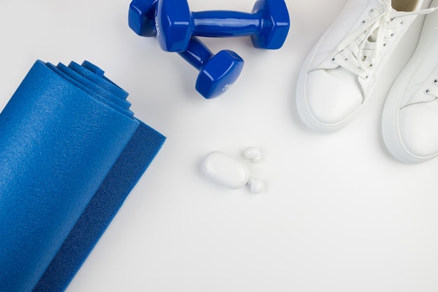 Concepto de accesorios de fitness Foto de pesas smartphone con auriculares zapatillas deportivas blancas estera sobre un fondo blanco con espacio vacío