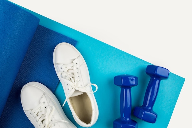 Concepto de accesorios de fitness Foto de pesas y zapatillas blancas sobre una alfombra deportiva sobre un fondo blanco con espacio vacío