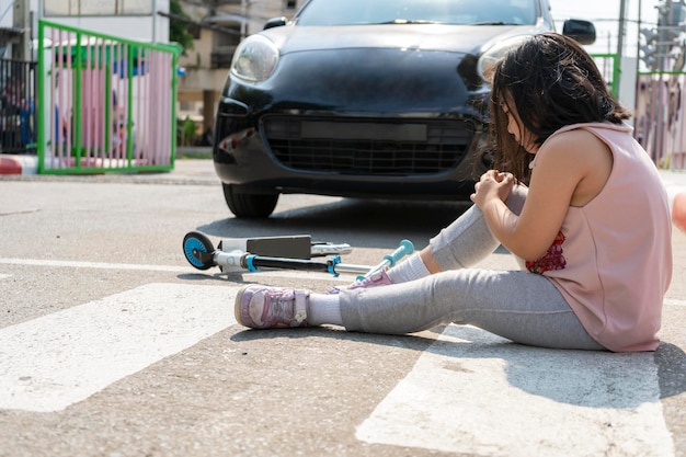 El concepto de un accidente causado por un niño que está jugando con un scooter y siendo atropellado por un automóvil Mientras usaba un paso de peatones La niña que sostenía la pierna lesionada por el accidente