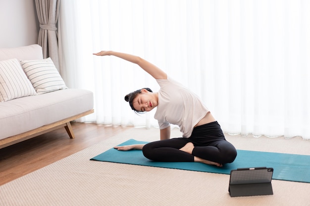 Concepto de actividad productiva una mujer adulta joven con una camiseta blanca practicando la flexibilidad de su cuerpo haciendo mat pilates.