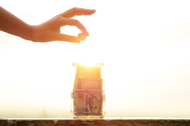 Concepto de acumular dinero en un frasco de vidrio a la luz del sol con la ayuda del sol