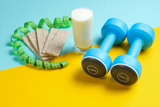 Concepto de adelgazamiento en forma. Pesas, regla, vaso de kéfir, pan de dieta en una mesa azul-amarilla