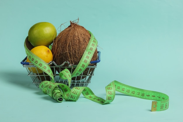 El concepto de adelgazamiento. Frutas tropicales y cinta métrica en la cesta de la compra sobre fondo azul. Alimentación saludable. Dieta de frutas. Vista superior
