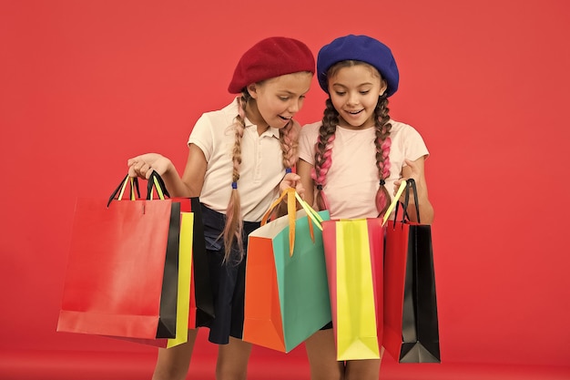 Concepto de adicto a las compras Signos de que eres adicto a las compras Los niños colegialas lindas sostienen un montón de bolsas de compras Alumnos de los niños satisfechos con las compras de fondo rojo Obsesionados con los centros comerciales y de ropa