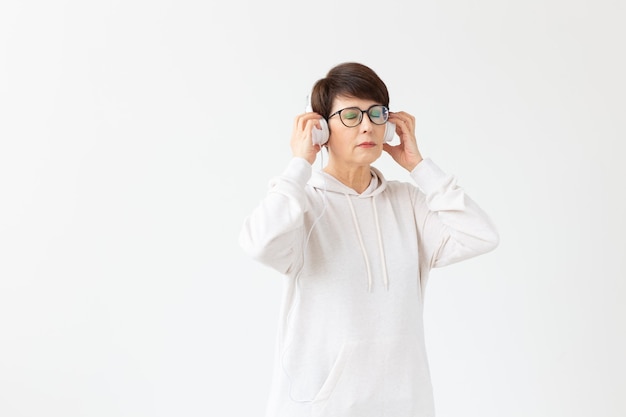 Concepto de afición, intereses y personas: hermosa mujer de 40 a 50 años escuchando música en auriculares grandes en una pared blanca con espacio de copia