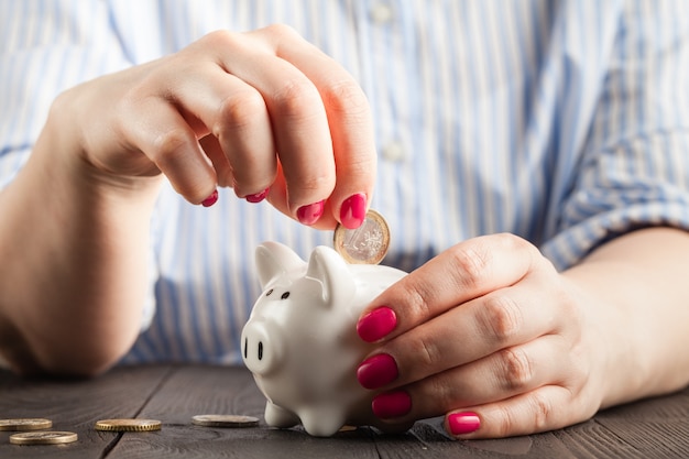 Concepto de ahorro, hucha blanca con mano humana femenina insertando monedas dentro