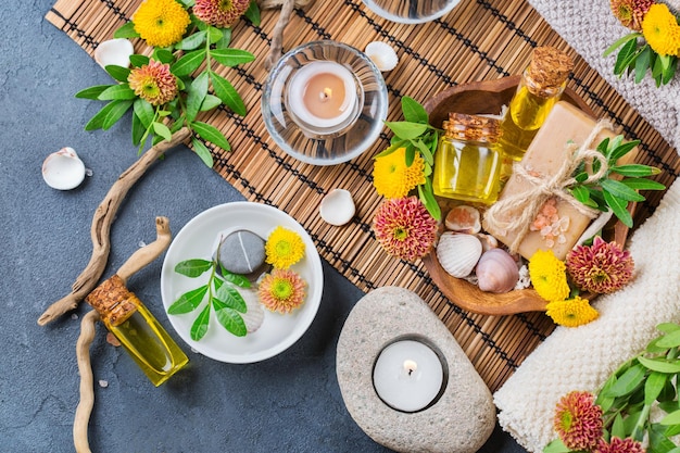 Concepto de ajuste de bienestar de naturaleza muerta de spa de otoño Otoño Surtido de crema de aceite esencial sal marina jabón natural velas flores de color naranja amarillo y toalla sobre una mesa negra Vista superior fondo plano