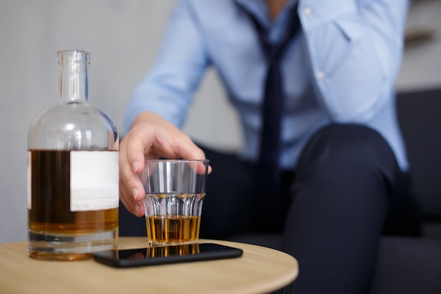 Concepto de alcoholismo, negocios y estrés - cerca de la botella de whisky y el vidrio en la mano del empresario