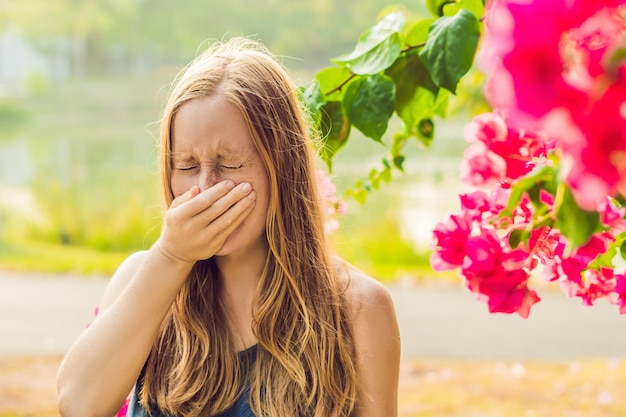 Concepto de alergia al polen joven va a estornudar árboles en flor en segundo plano.