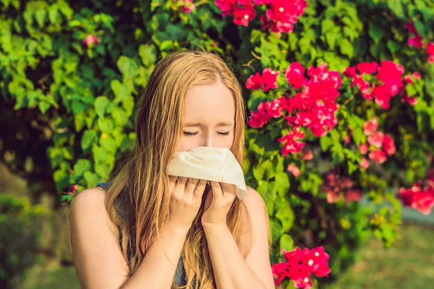 Concepto de alergia al polen joven va a estornudar árboles en flor en segundo plano.