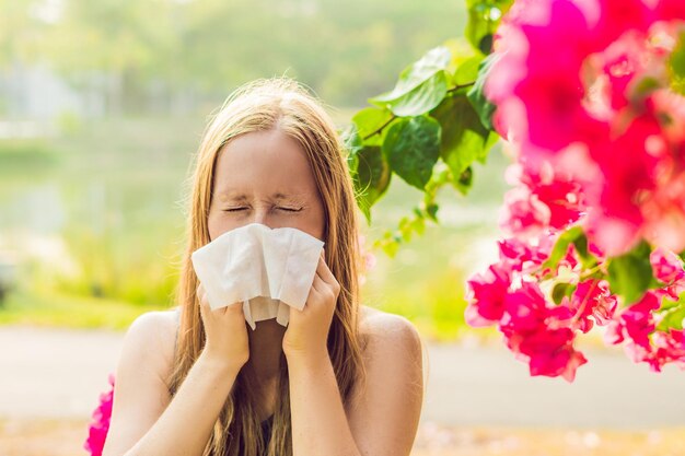 Concepto de alergia al polen joven va a estornudar árboles en flor en segundo plano.