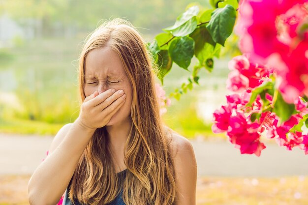 Concepto de alergia al polen. La mujer joven va a estornudar. Árboles en flor en segundo plano.