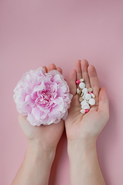 Concepto de alergia Peonía rosa y pastillas surtidas en manos de mujer sobre un fondo rosa