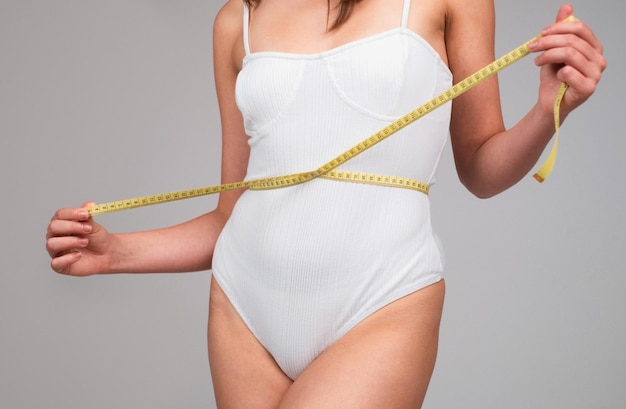 Concepto de alimentación y dieta saludables Chica joven con cintura perfecta con una cinta métrica Cuidado del cuerpo