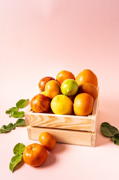 Concepto de alimentación saludable Cítricos en una caja de madera sobre un fondo rosa.