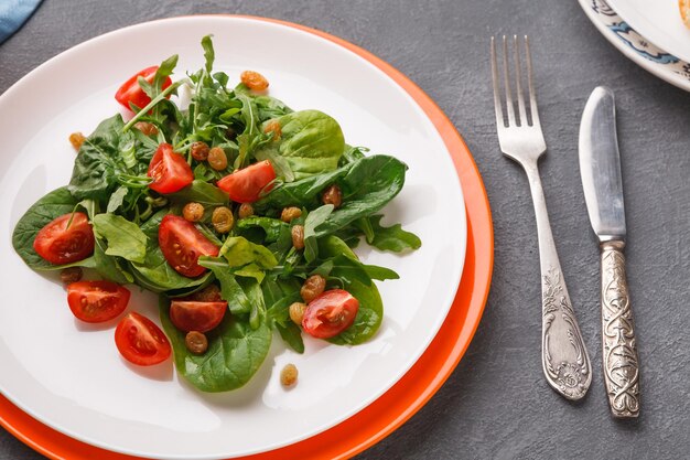 Concepto de alimentación saludable. Ensalada fresca con verduras, tomates y pasas sobre fondo gris. Vegetales orgánicos.