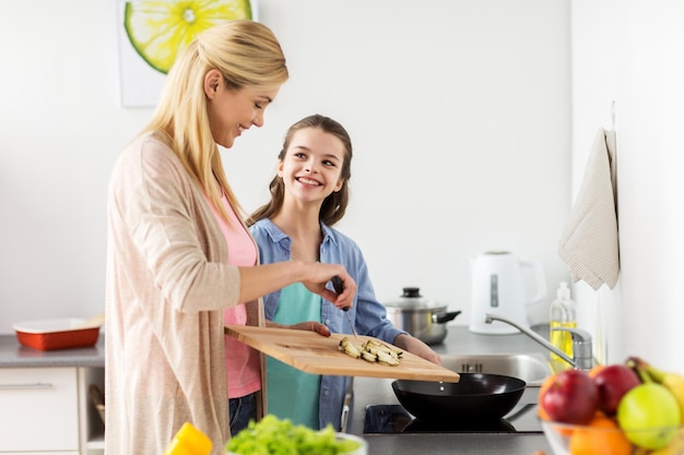 Foto concepto de alimentación saludable, familia y personas: madre e hija felices cocinando y friendo comida para la cena en la cocina de casa