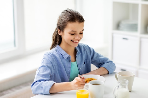 concepto de alimentación saludable, familia y personas: niña feliz desayunando copos de maíz en la cocina de casa