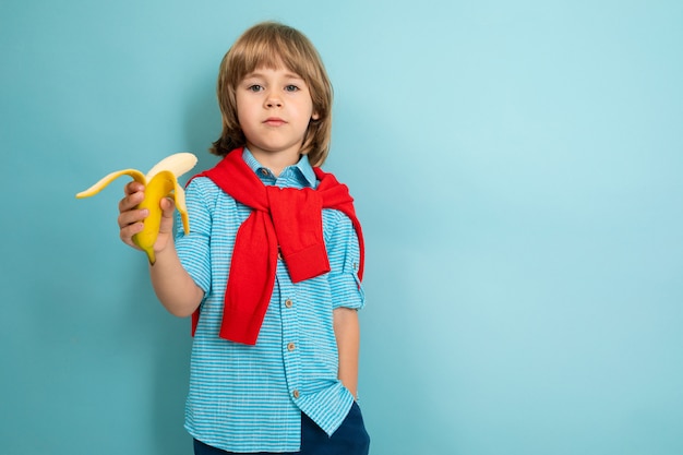 Concepto de alimentación saludable Un niño con una camisa de manga corta sostiene un plátano mordido sobre un fondo azul claro