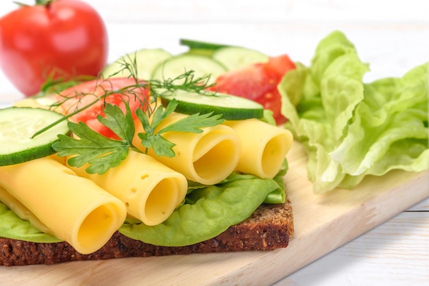 Concepto de alimentación saludable sándwich fresco y multicolor con pan integral oscuro y queso lechuga tomate pepino eneldo cebolla tierna sobre tabla de madera en primer plano
