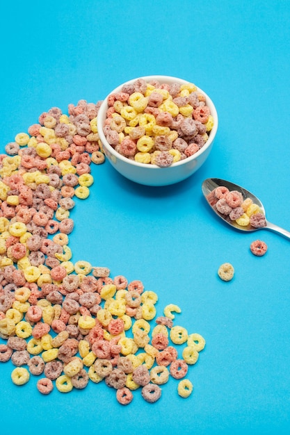 Foto concepto de alimentos saludables cereal de anillo colorido en un cuenco con cuchara y arreglado sobre un fondo azul claro