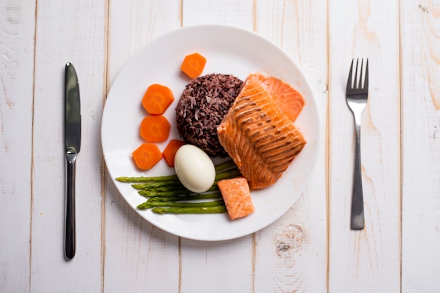 Concepto de alimentos saludables, salmón con arroz y vegetales sobre fondo de madera