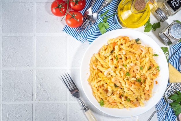 Concepto de almuerzo mediterráneo italiano Pasta fusilli con mariscos, camarones, verduras y salsa cremosa En una mesa de azulejos blancos con especias para la cena, espacio para copiar