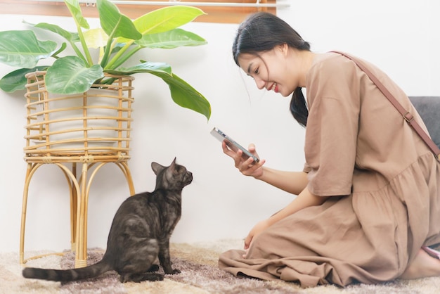 Concepto de amante de las mascotas Mujer asiática joven que usa un teléfono inteligente para tomar una foto del gato en la sala de estar