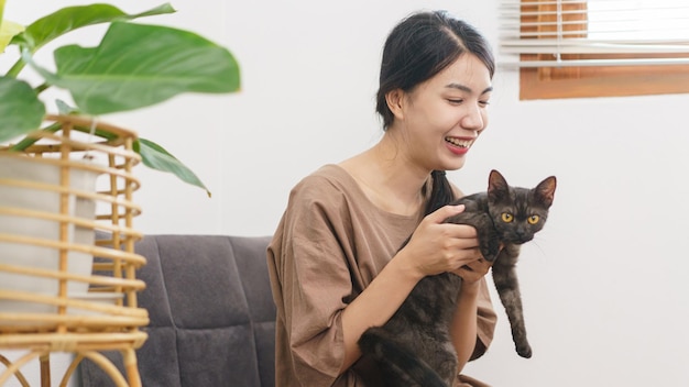 Concepto de amante de las mascotas Mujer asiática joven sentada para relajarse en el sofá en el piso para jugar y abrazar al gato