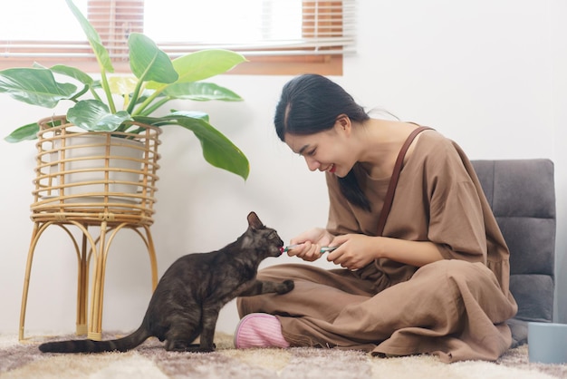 Concepto de amante de las mascotas Mujer asiática joven sentada en un sofá en el suelo para alimentar al gato con una golosina cremosa en casa