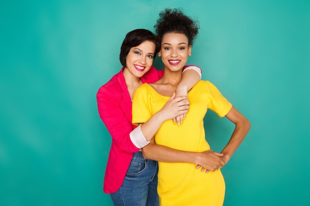 Concepto de amistad y apoyo multiétnico. Chicas mulatas y caucásicas en ropa casual colorida abrazándose y divirtiéndose en el fondo azul del estudio con espacio de copia