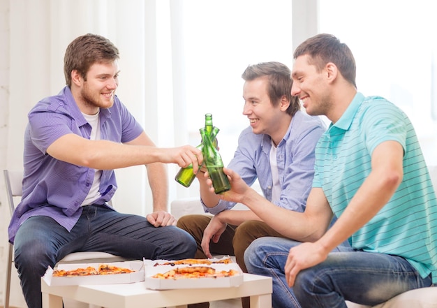 concepto de amistad, comida y ocio - amigos varones sonrientes con cerveza y pizza en casa