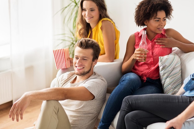 Foto concepto de amistad, comunicación, personas y entretenimiento - amigos felices con cerveza y palomitas de maíz hablando y viendo televisión en casa