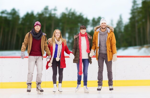 concepto de amistad, deporte y ocio - amigos felices tomados de la mano en la pista de patinaje sobre fondo al aire libre