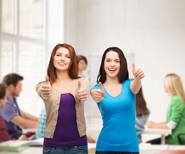 concepto de amistad, educación y gente feliz - dos chicas sonrientes mostrando los pulgares hacia arriba