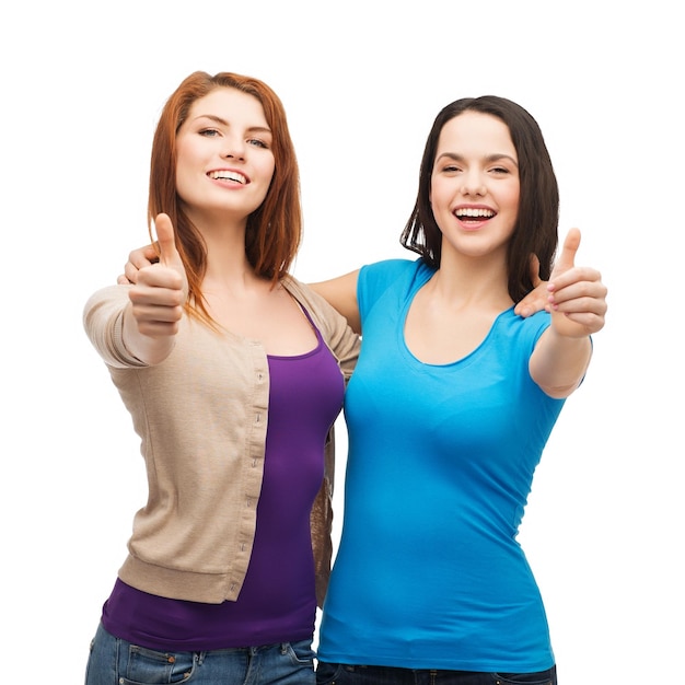 Foto concepto de amistad y gente feliz - dos chicas sonrientes mostrando los pulgares hacia arriba