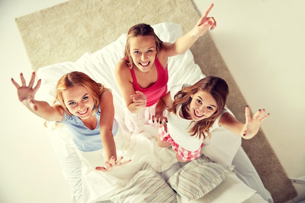 concepto de amistad, gente y fiesta de pijamas - amigos felices o adolescentes divirtiéndose, bailando y saltando en la cama en casa
