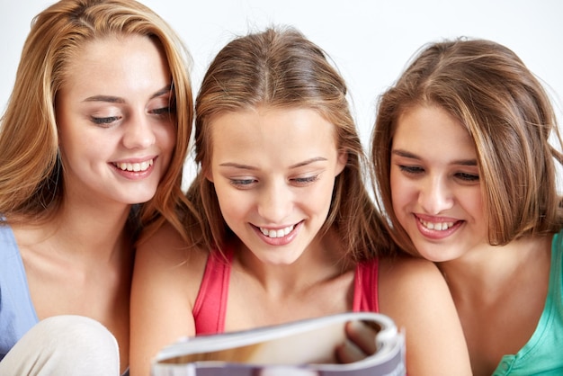 concepto de amistad, gente y fiesta de pijamas - amigos felices o adolescentes leyendo revistas en casa