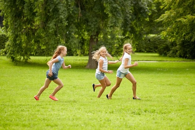 concepto de amistad, infancia, ocio y personas - grupo de niños felices o amigos jugando juegos de recuperación y corriendo en el parque de verano