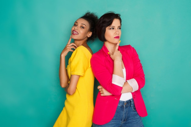 Concepto de amistad multiétnica. Chicas mulatas y caucásicas en ropa casual colorida posando en el fondo azul del estudio con espacio de copia