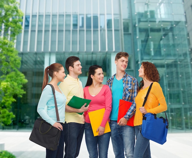 concepto de amistad, negocios, educación y personas - grupo de adolescentes sonrientes con carpetas y mochilas escolares sobre el fondo del campus